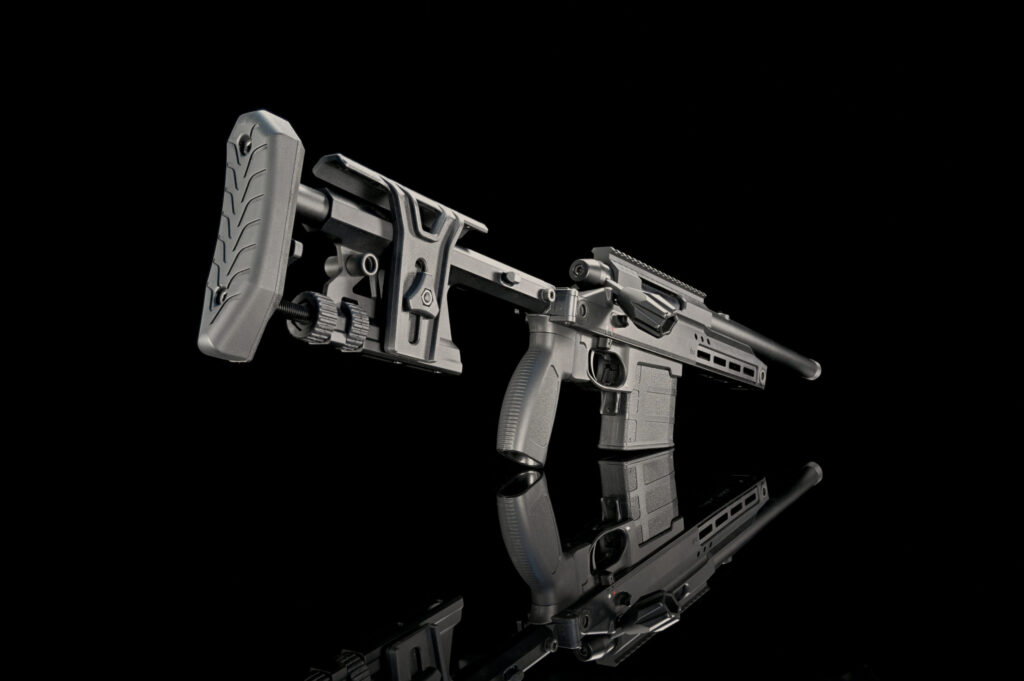 Close-up view of a tactical firearm's rear section, highlighting its textured buttstock, intricate mechanics, and ergonomic grip, set against a dark reflective background.